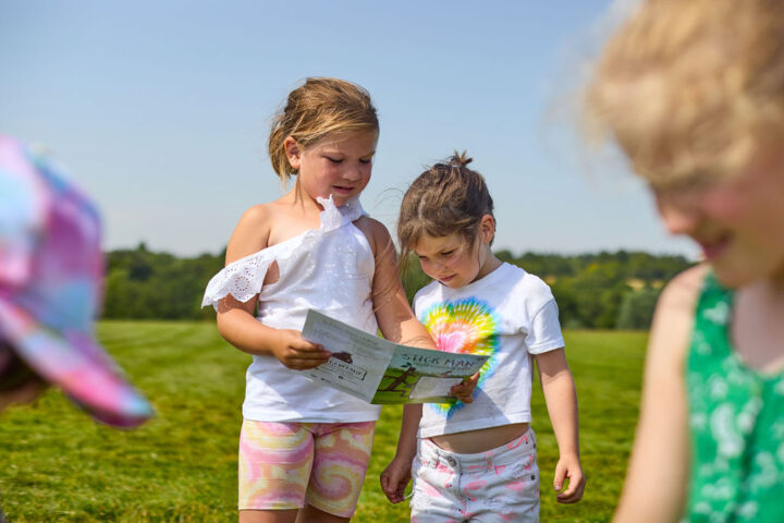 Small group of girls in summer clothes look at a Stick Man leaflet in the park