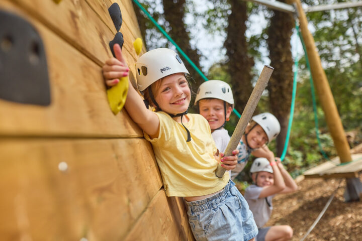 Small group of children wearing white helmets leaning on a climbing wall