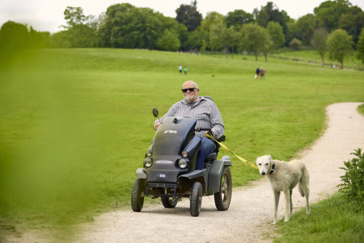 Man on a mobility scooter and his dog in parkland