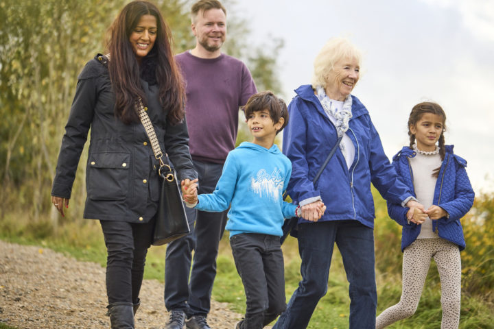 Five people in a family walking in a park holding hands