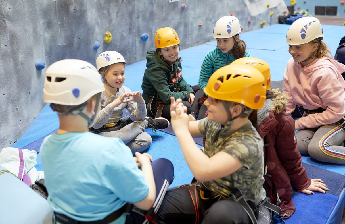 Children sitting near a climbing wall